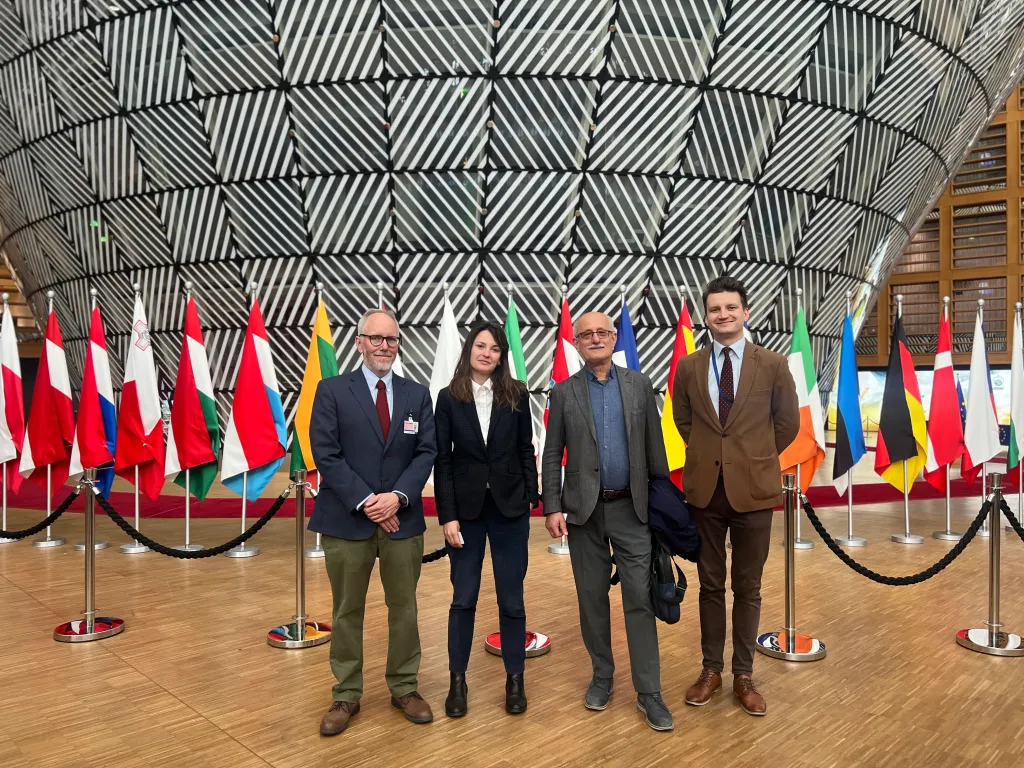 four people posing in the European Parliament in front of the flags